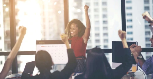 woman in an office punching the air with onlookers celebrating 