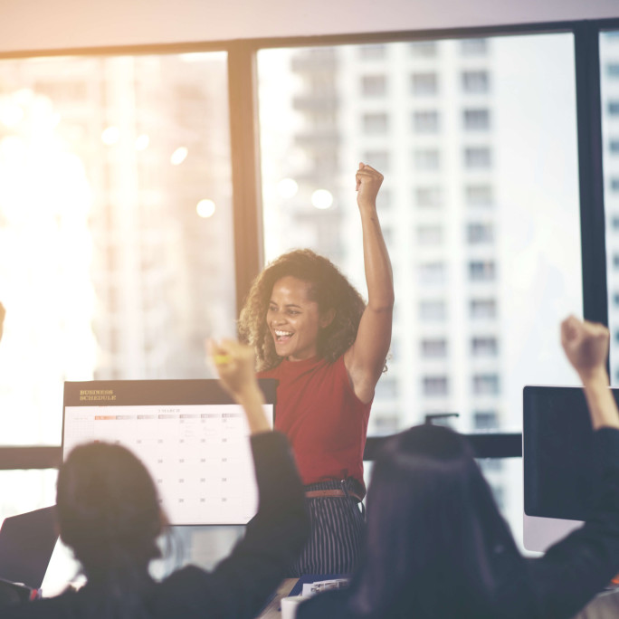 woman in an office punching the air with onlookers celebrating