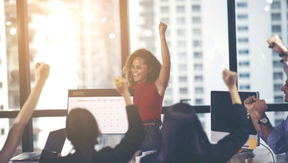 woman in an office punching the air with onlookers celebrating