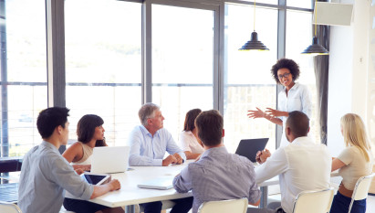 woman leading meeting with seven other people sitting at a table