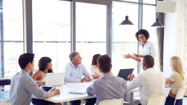 woman leading meeting with seven other people sitting at a table
