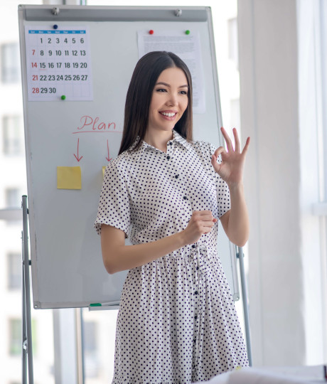 woman presenting in front of laptop with whiteboard behind