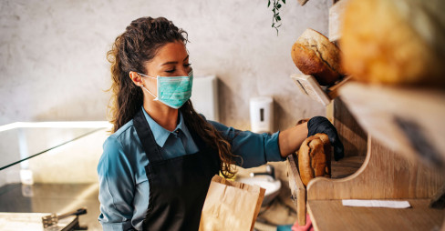 woman with mask on placing bread in a bag