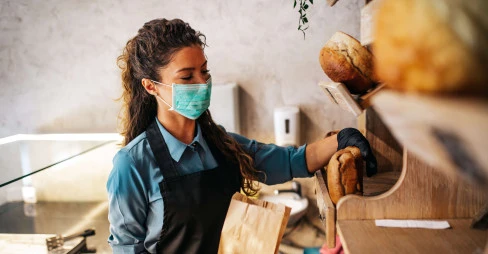 woman with mask on placing bread in a bag