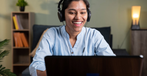 woman in blue shirt smiling at laptop wearing a headset