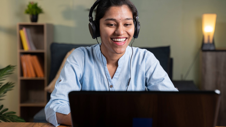 woman in blue shirt smiling at laptop wearing a headset