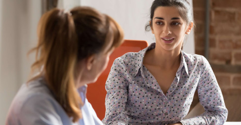 eye level view of woman in smart clothing speaking to another woman at a desk