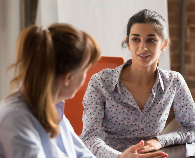 eye level view of woman in smart clothing speaking to another woman at a desk