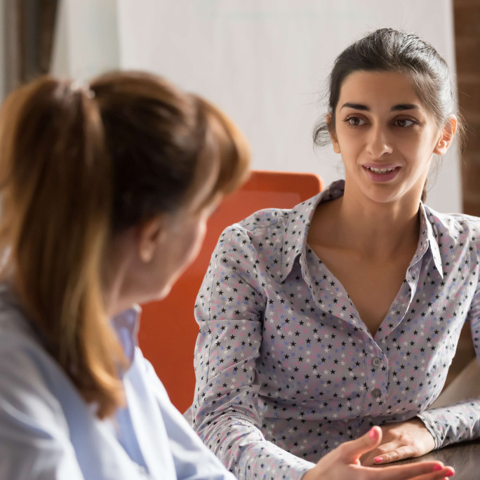 eye level view of woman in smart clothing speaking to another woman at a desk