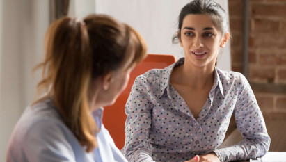 eye level view of woman in smart clothing speaking to another woman at a desk