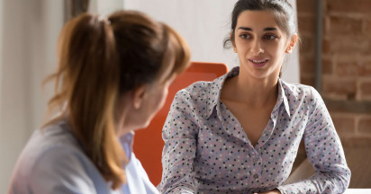 eye level view of woman in smart clothing speaking to another woman at a desk